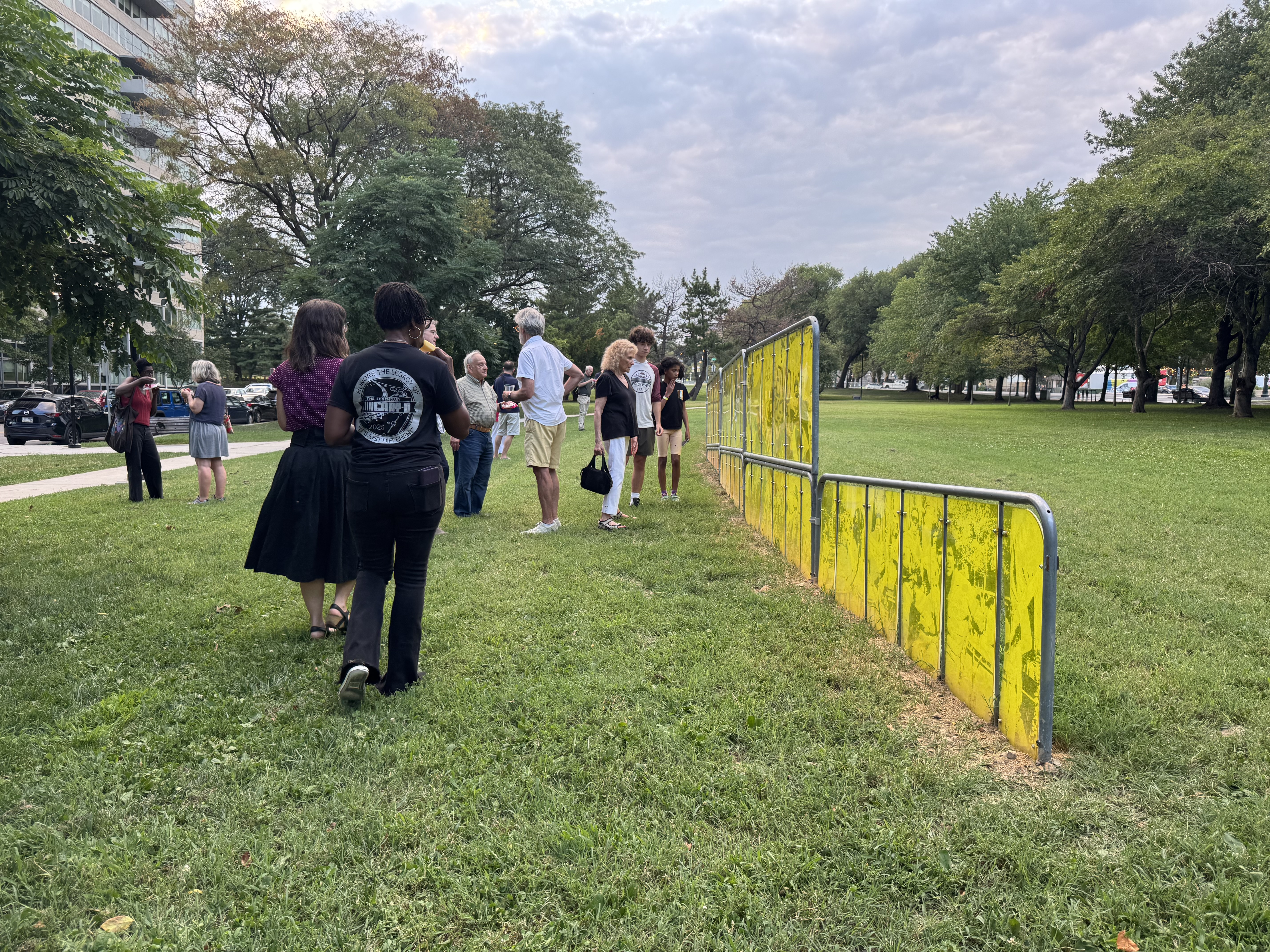 Open green space with a group of nine people looking at yellow panels filled with art.