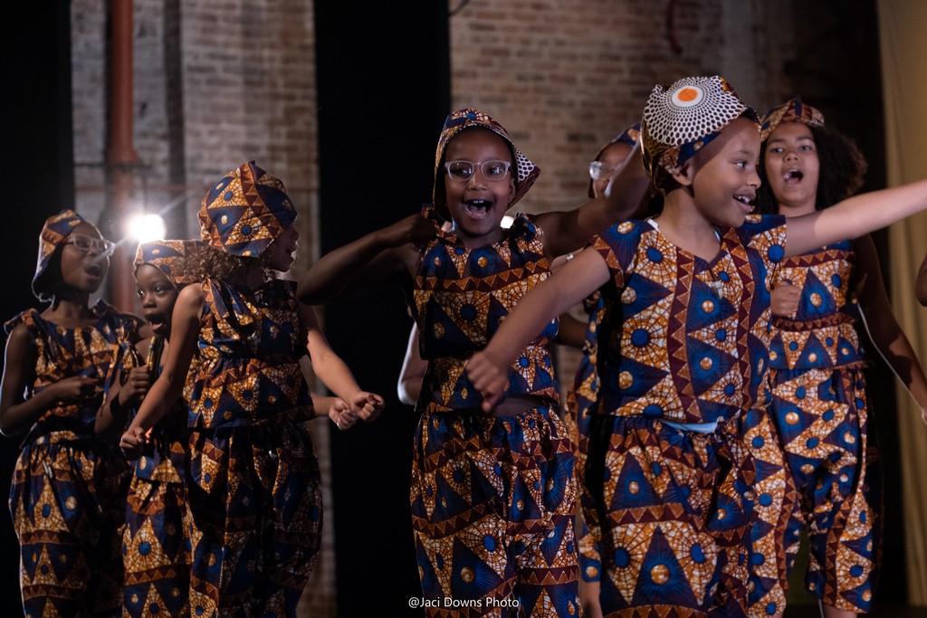 Group of six young Black girls in traditional African garb dancing.