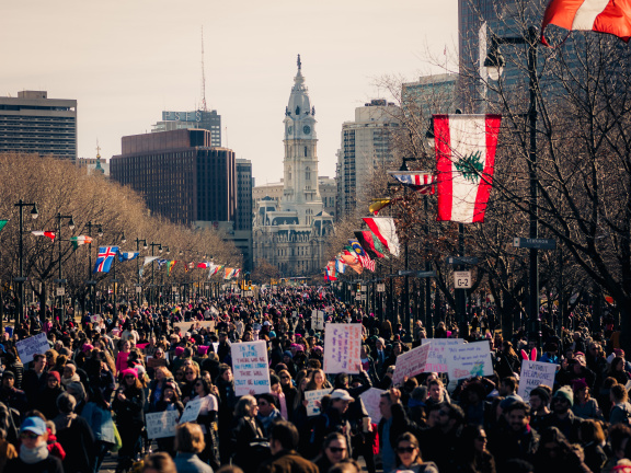Large group of people protesting on Benjamin Franklin Parkway in Philadelphia with City Hall in the distance.