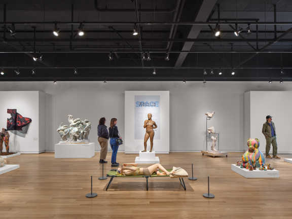 Large, open art gallery space featuring sculpted human bodies and two gallery visitors viewing the art.