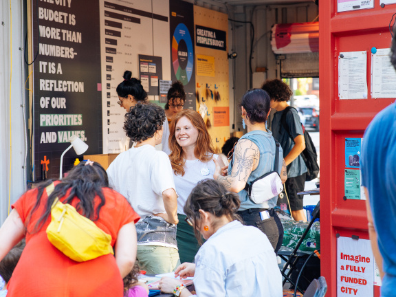Group of young women mingling in front of the red shipping container that is the People's Budget Office in Love Park.