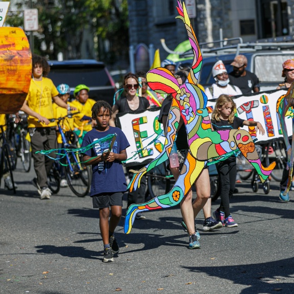 Group of community members marching in Spiral Q's Peoplehood Parade in West Philadelphia with  art work, puppets, and banners.
