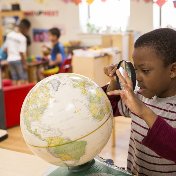 Small child looking at globe through magnified glass