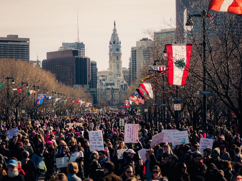Large group of people protesting on Benjamin Franklin Parkway in Philadelphia with City Hall in the distance.