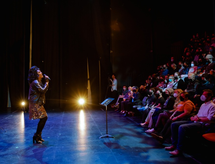 Black drag performer in sparkled skirt singing to crowded audience at Miniball Performance.