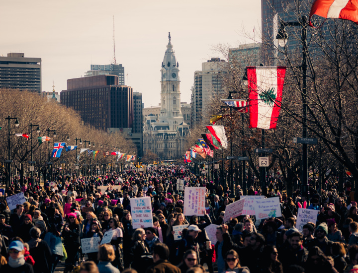 Large group of people protesting on Benjamin Franklin Parkway in Philadelphia with City Hall in the distance.