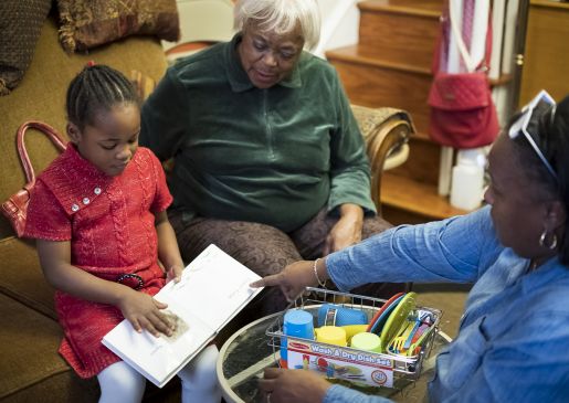 a child reads with her grandmother and home visitor